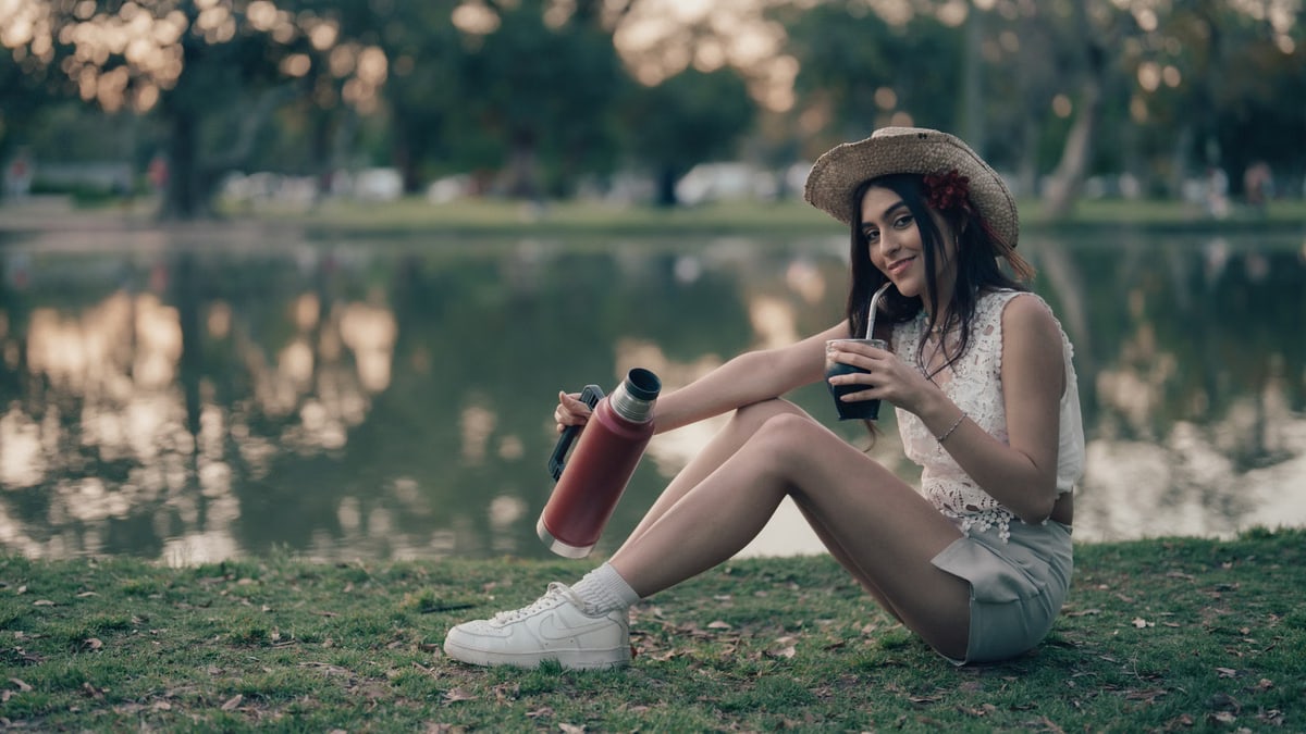 Young woman sitting by a lake drinking mate outdoors in Buenos Aires, Argentina.