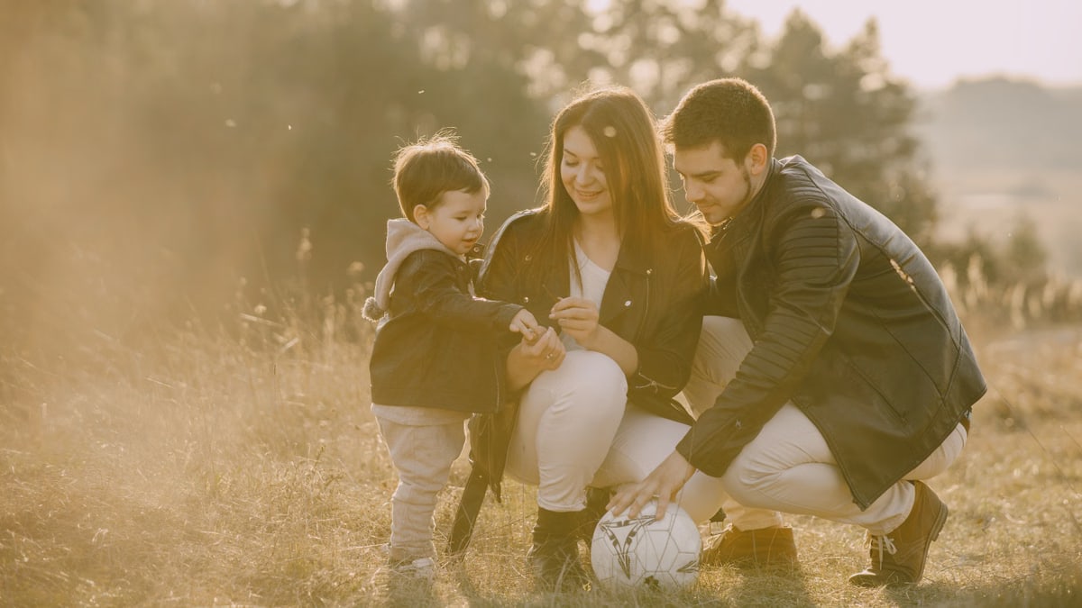 A cheerful family bonding outdoors with a soccer ball, enjoying a sunny day in the grass.